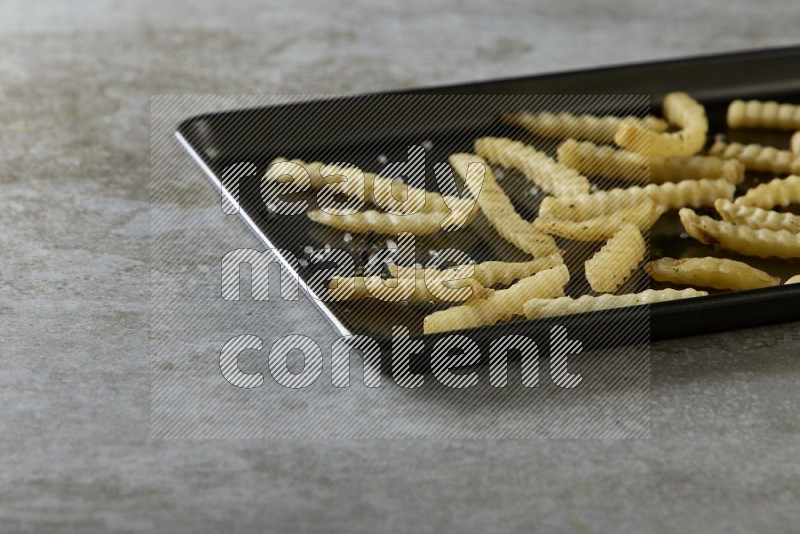 crinkle fries in a black stainless steel rectangle tray on grey textured counter top