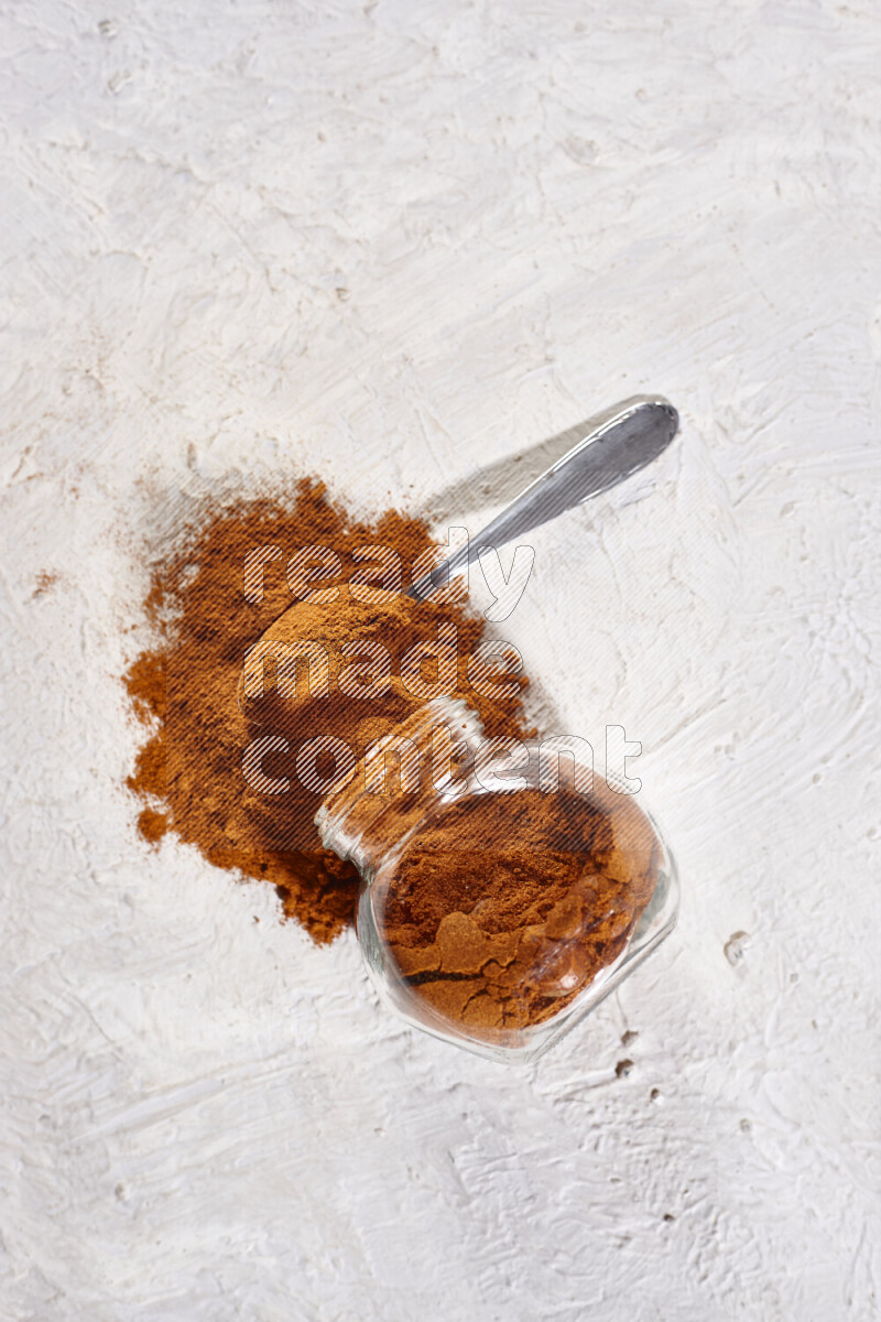 A glass jar full of ground paprika powder flipped with some spilling powder on white background