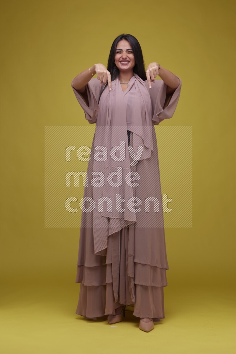 A woman Pointing on a Yellow Background wearing Brown Abaya