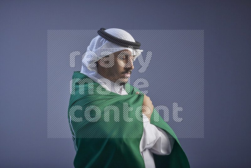 رجل سعودي يرتدي ثوب وشماغ ابيض يلف علم سعودي كبير على كتفه