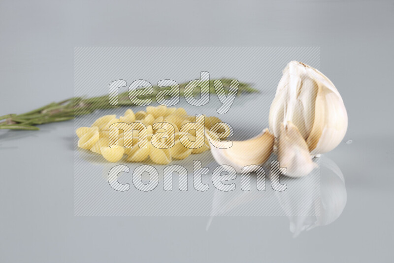Raw pasta with different ingredients such as cherry tomatoes, garlic, onions, red chilis, black pepper, white pepper, bay laurel leaves, rosemary, cardamom and mushrooms on light blue background