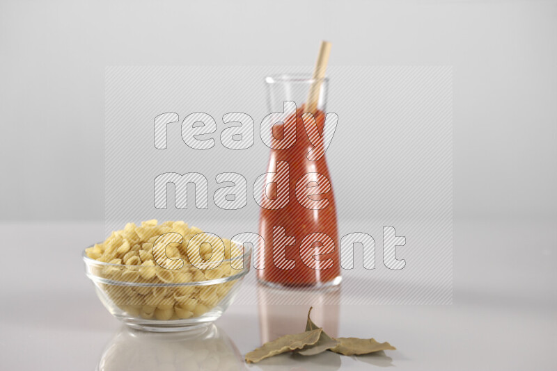 Raw pasta with tomatoe pasta with different ingredients such as cherry tomatoes, basil, garlic, bay laurel, cardamom, white pepper, black pepper, red chilis and wheat stalks on light grey background