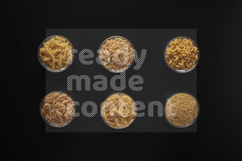Different pasta types in 6 glass bowls on black background