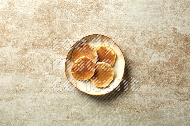 Four stacked plain mini pancakes in an irregular plate on beige background