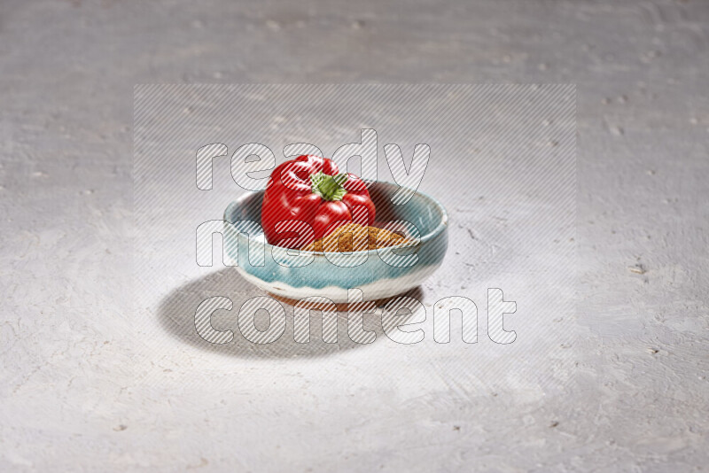 A colored pottery plate full of ground paprika powder and red bell pepper on white background