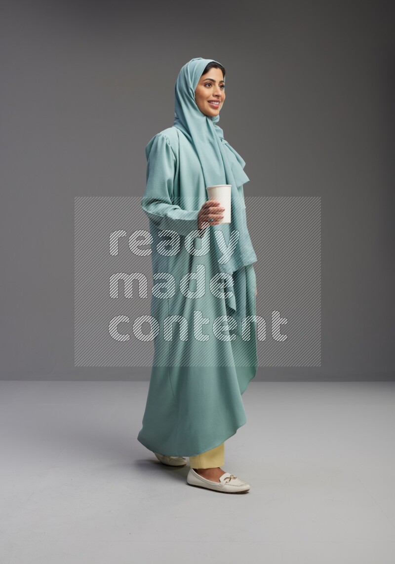 Saudi Woman wearing Abaya standing  holding paper cup on Gray background