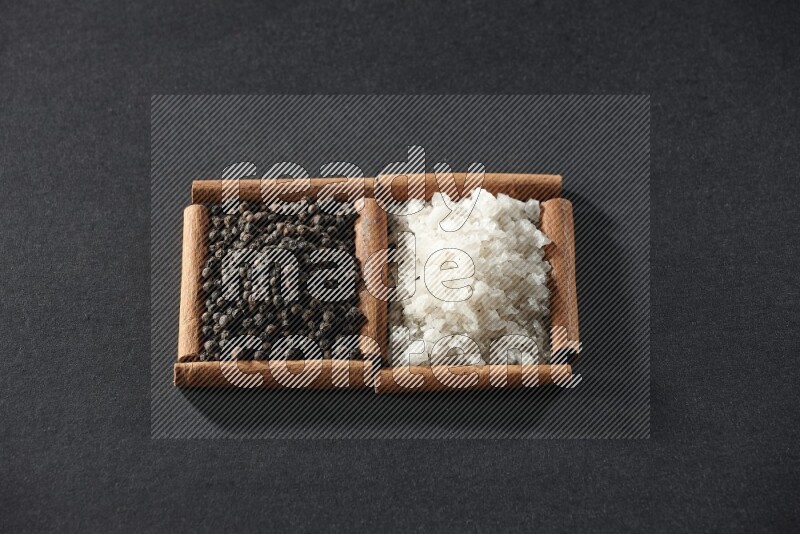 مربعان من أعواد القرفة ممتلئان بالملح الأبيض وحبوب الفلفل الأسود علي خلفية سوداء