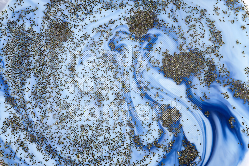 A close-up of sparkling gold glitter scattered on swirling blue background