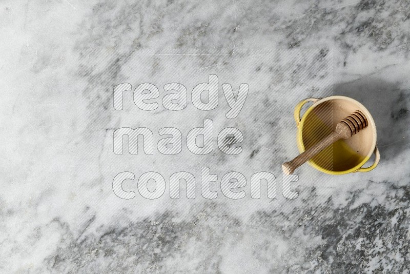 Multicolored Pottery Bowl with wooden honey handle in it, on grey marble flooring, Top View