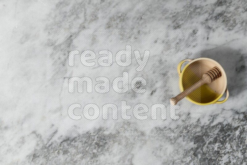 Multicolored pottery bowl with wooden honey dipper in it on grey marble background