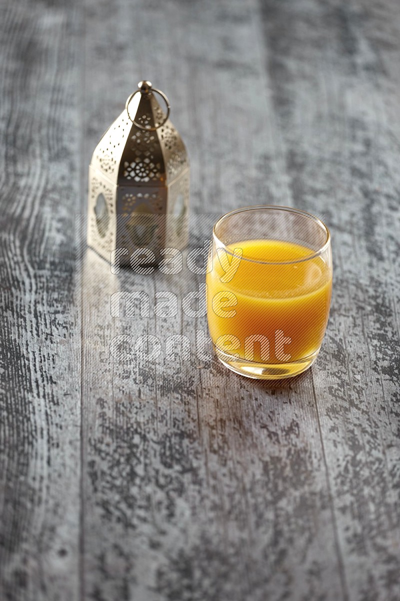 A silver lantern with different drinks, dates, nuts, prayer beads and quran on grey wooden background