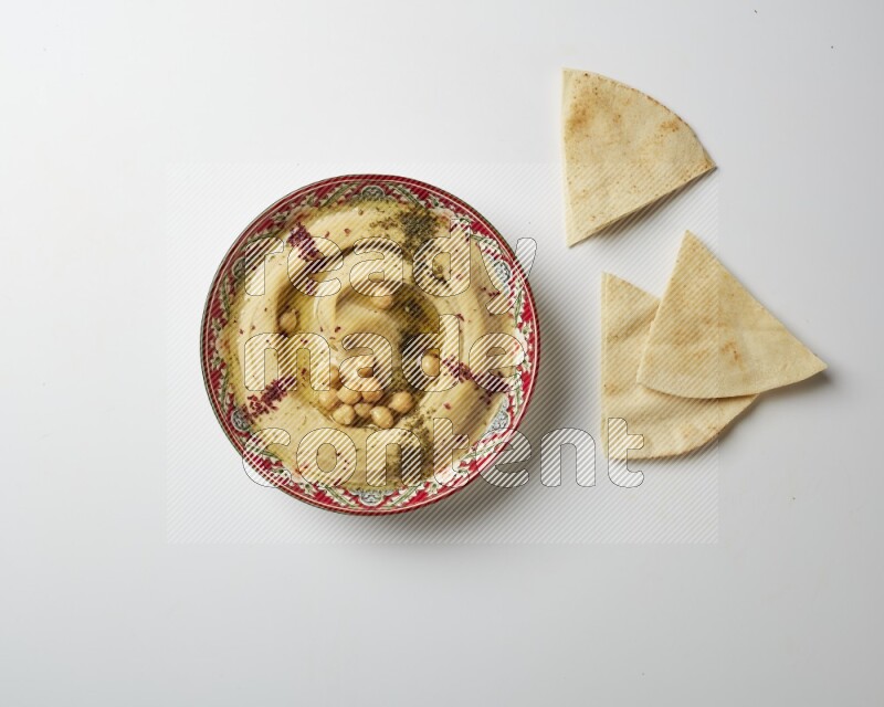 Hummus in a red plate with patterns garnished with zaatar & sumak on a white background