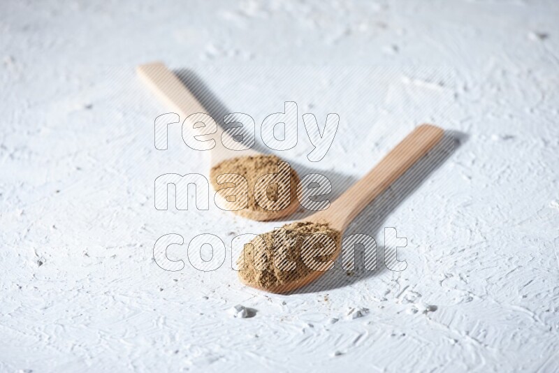 Wooden spoons full of allspice powder and allspice whole balls spreaded on a textured white flooring