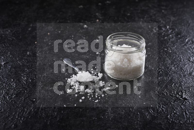 A glass jar full of coarse sea salt crystals on black background