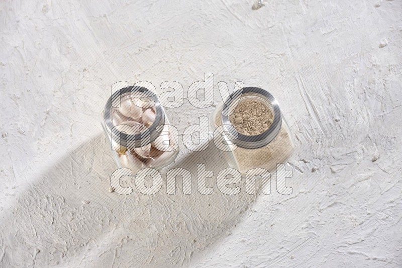 2 glass spice jars full of garlic powder and cloves on a textured white flooring in different angles
