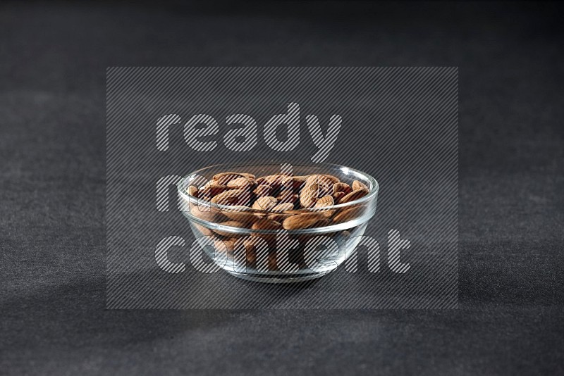 A glass bowl full of peeled almonds on a black background in different angles