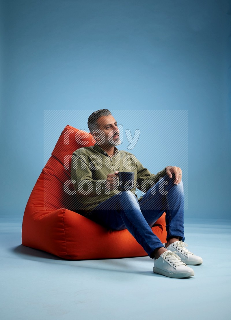A man sitting on an orange beanbag and drinking coffee