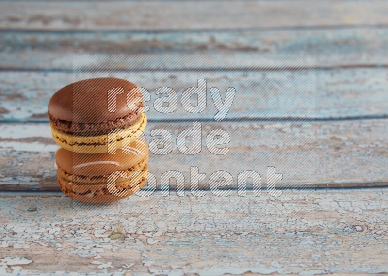 45º Shot of of two assorted Brown Irish Cream, and Yellow, and Brown Chai Latte macarons  on light blue background