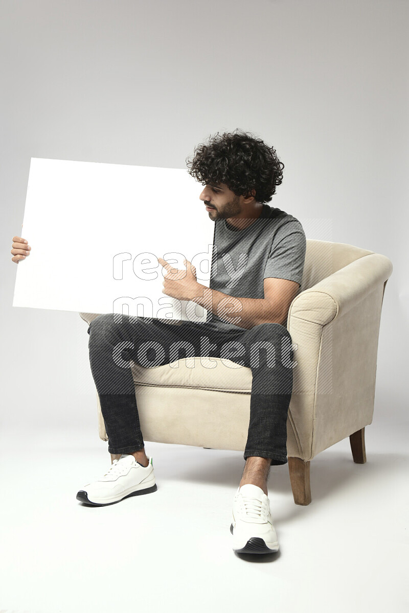 A man wearing casual sitting on a chair holding a white board on white background