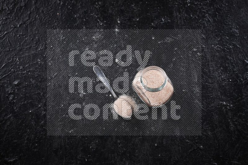 A glass jar full of fine himalayan salt on black background