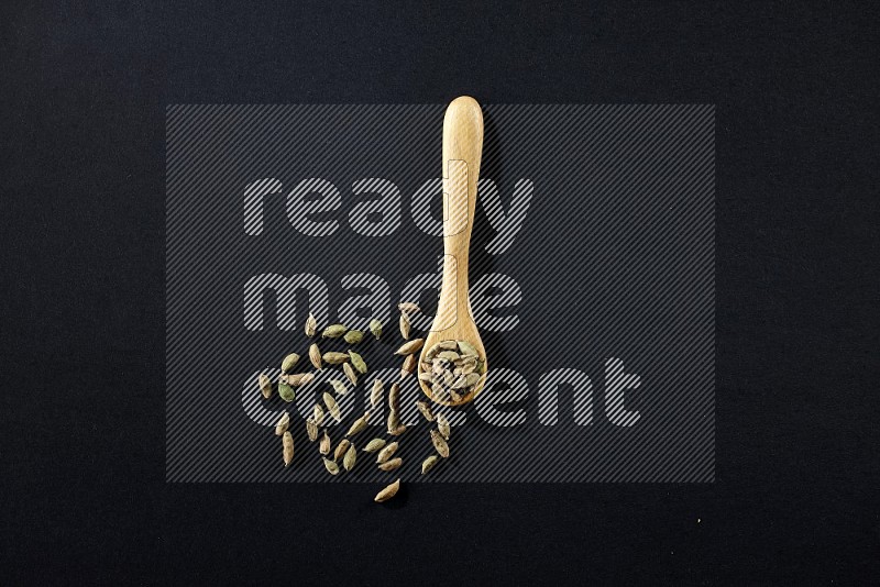 A wooden spoon full of cardamom on black flooring