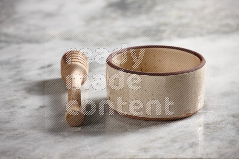 Beige Pottery Oven Bowl with wooden honey handle on the side with grey marble flooring, 15 degree angle