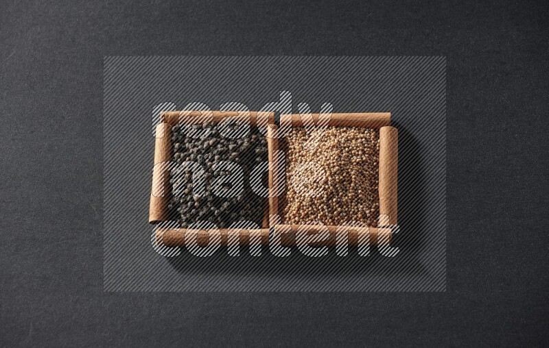 مربعان من أعواد القرفة ممتلئان بحبوب الخردل وحبوب الفلفل الأسود علي خلفية سوداء