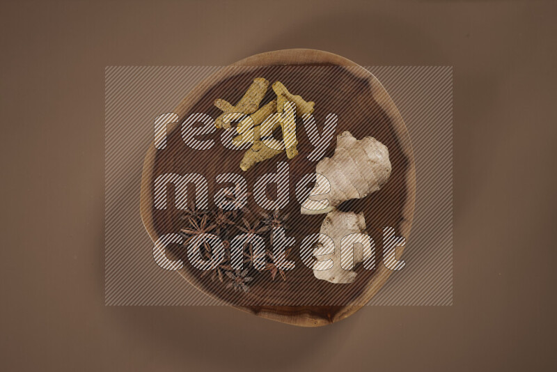 An assorted whole spices on a flat wooden tray including fresh and dried ginger, cinnamon sticks, cardamom, turmeric fingers, cloves, star anise on beige background