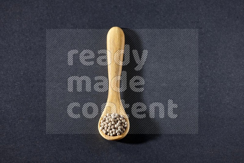 A wooden spoon full of white pepper beads on black flooring