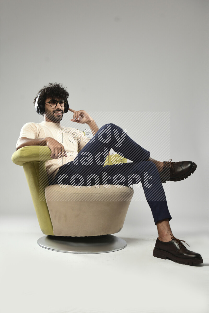 رجل يرتدي ملابس كاجوال يجلس علي كرسي و يضع سماعات رأس علي خلفية بيضاء