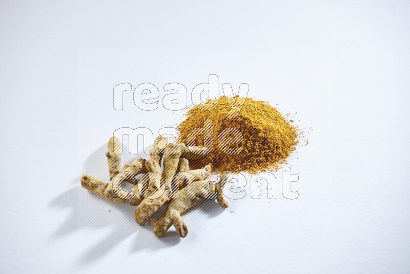 Turmeric powder and dried turmeric whole fingers on white flooring