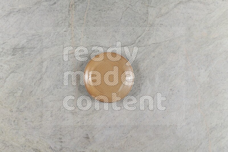 A circular beige pottery plate on grey marble background
