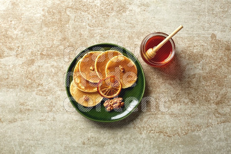 Five stacked dried orange mini pancakes in a green plate on beige background