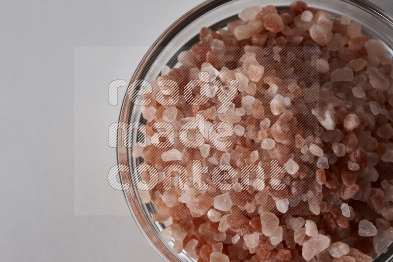 A glass bowl full of coarse himalayan salt crystals on white background
