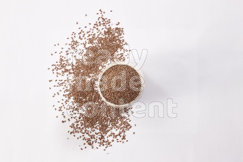 A pottery beige bowl full of flax seeds and more seeds spread on a white flooring