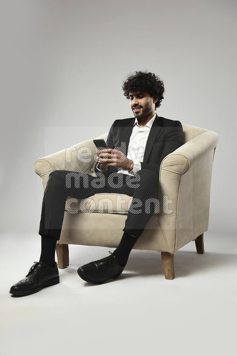 A man wearing formal sitting on a chair browsing on the phone on white background