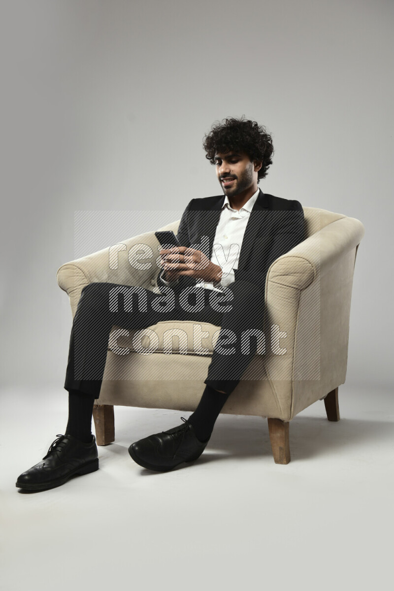 A man wearing formal sitting on a chair browsing on the phone on white background