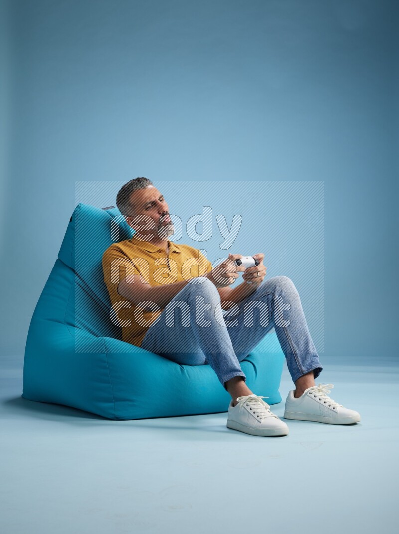 A man sitting on a blue beanbag and gaming with joystick