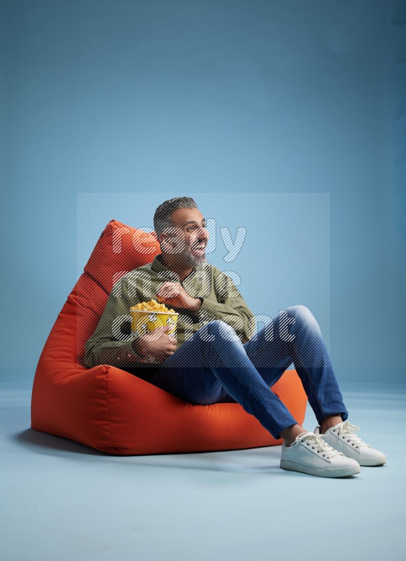 A man sitting on an orange beanbag and eating popcorn
