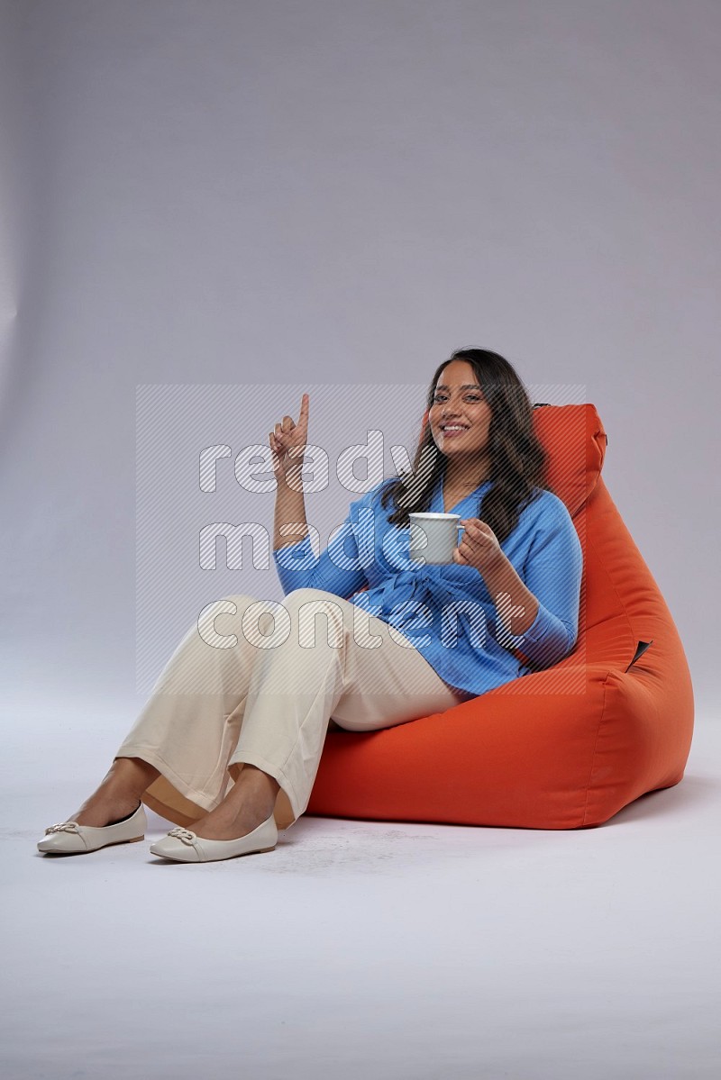 A woman sitting on an orange beanbag and drinking coffee