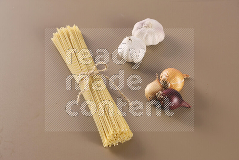 Raw pasta with different ingredients such as cherry tomatoes, garlic, onions, red chilis, black pepper, white pepper, bay laurel leaves, rosemary and cardamom on beige background