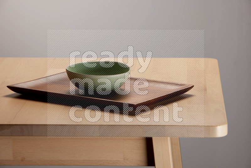 green bowl placed on a rectangular wooden tray on the edge of wooden table