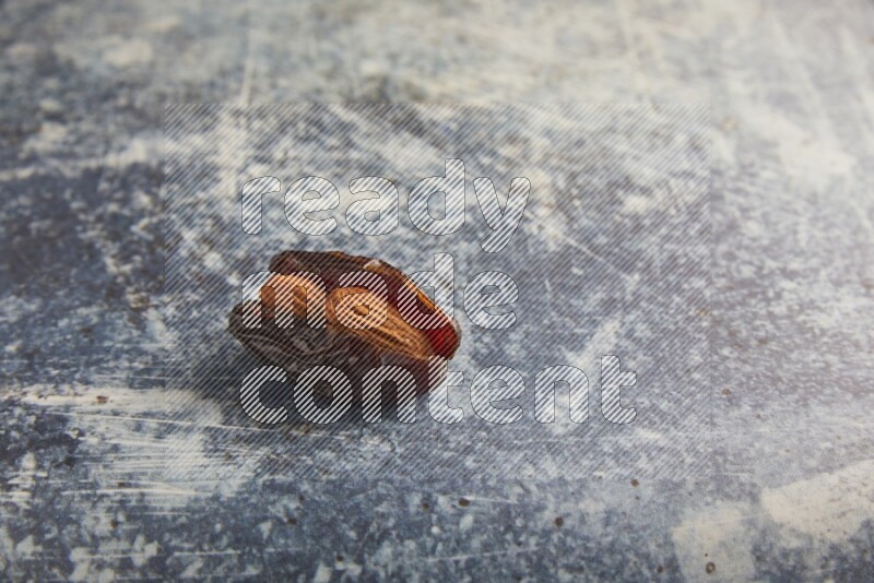 one almond stuffed madjoul dates on a rustic blue background