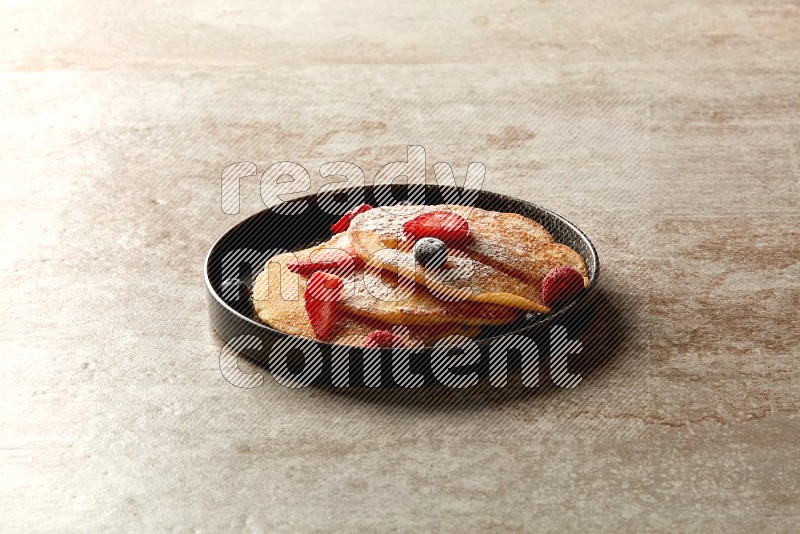 Three stacked mixed berries pancakes in a black plate on beige background