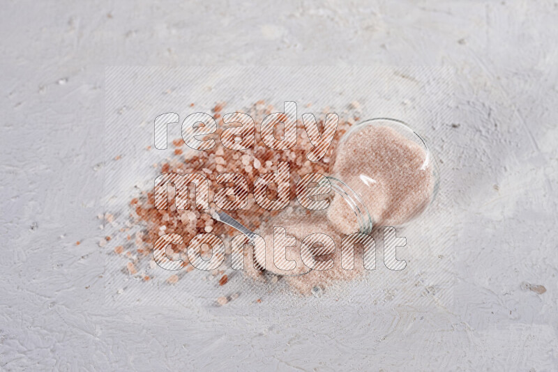 A glass jar full of fine himalayan salt with some himalayan crystals beside it on a white background
