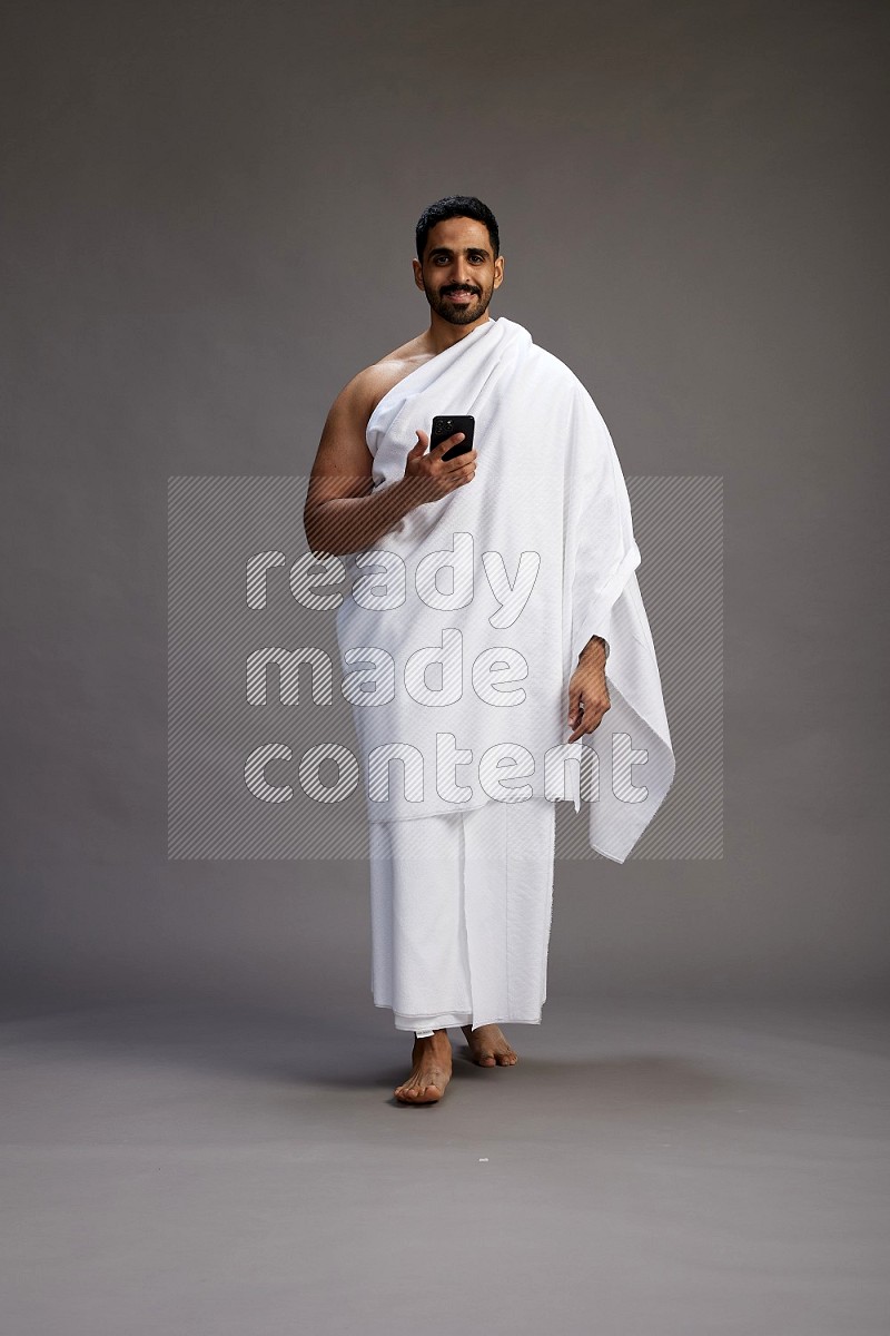 A man wearing Ehram Standing texting on phone on gray background
