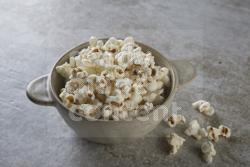 popcorn in a off-white handheld ceramic bowl on a grey textured countertop