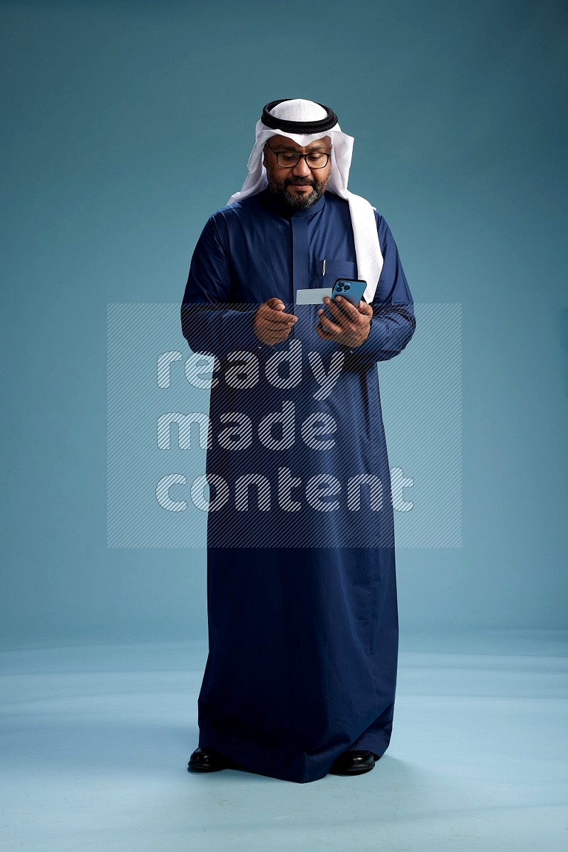Saudi Man with shimag Standing holding ATM card while talking on phone on blue background