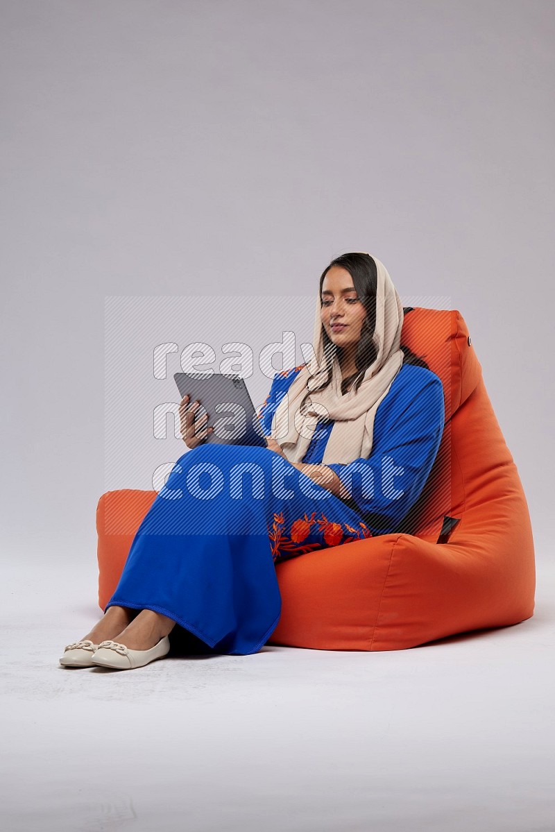 A Saudi woman sitting on an orange beanbag and working on tablet