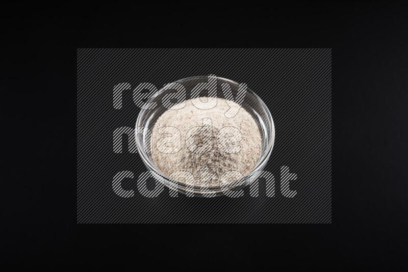 A glass bowl full of onion powder on black background